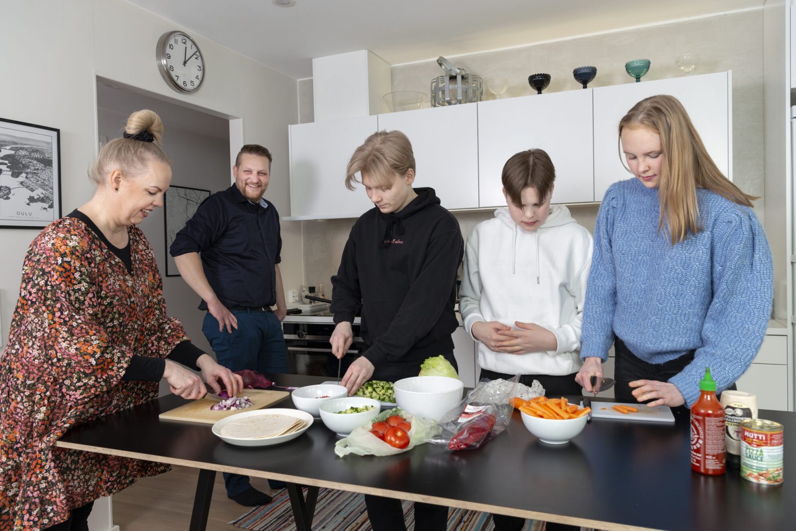 Mies, nainen ja kolme nuorta keittiössä laittamassa ruokaa.