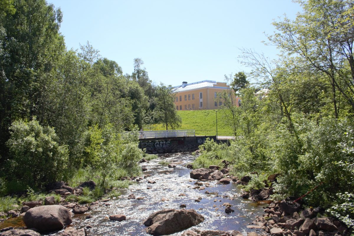 Koski ja silta, taustalla kaksikerroksinen rakennus.