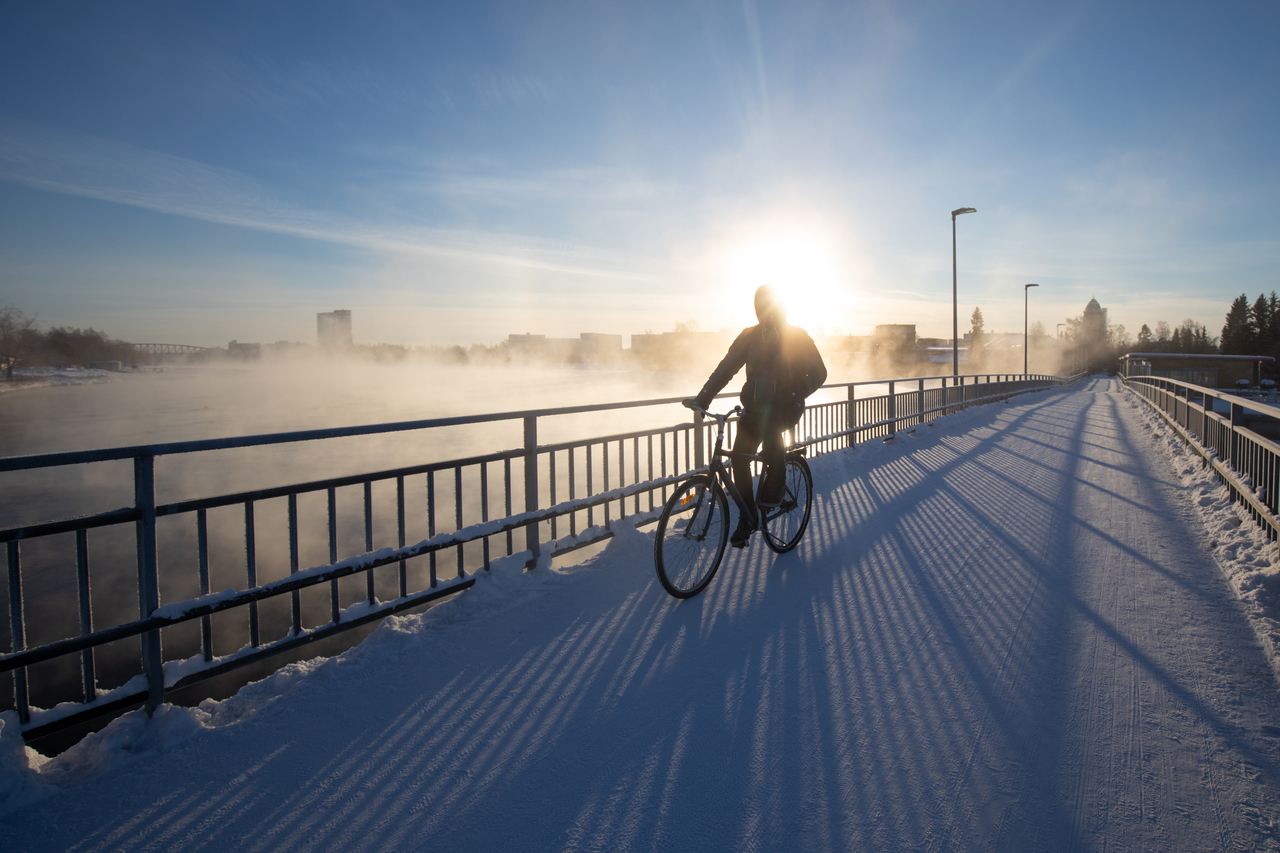 Pyöräilijä sillalla talvella auringonpaisteessa.