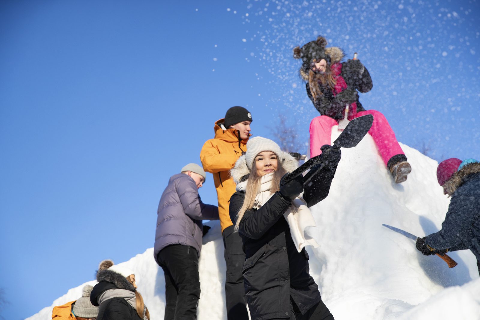 several young people around a snow pile making a snow sculpture