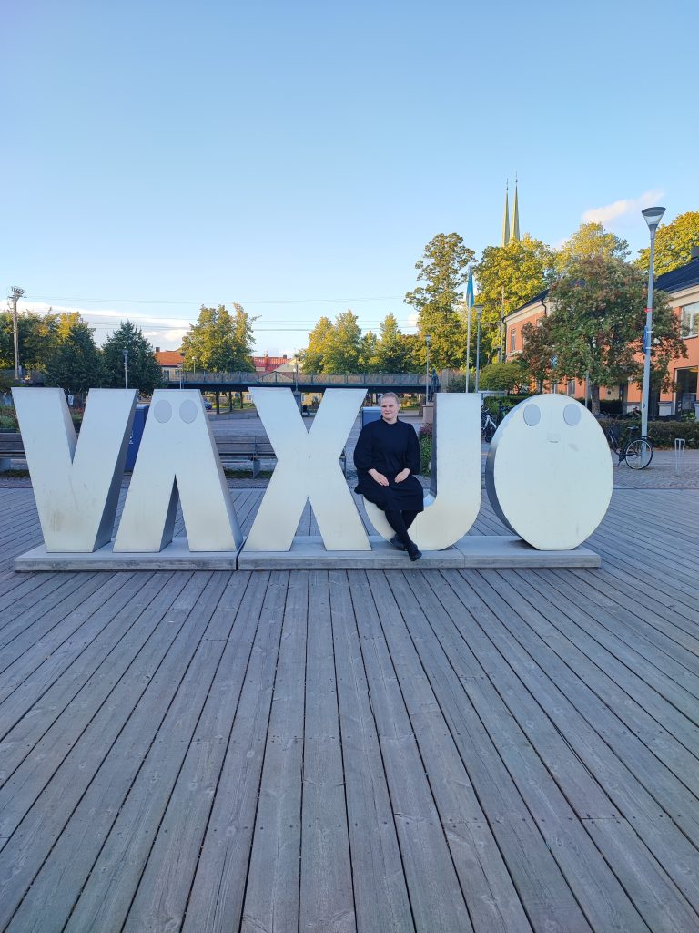 Kuva kirjoittajasta istumassa Växjö-kirjainpatsaan äärellä.