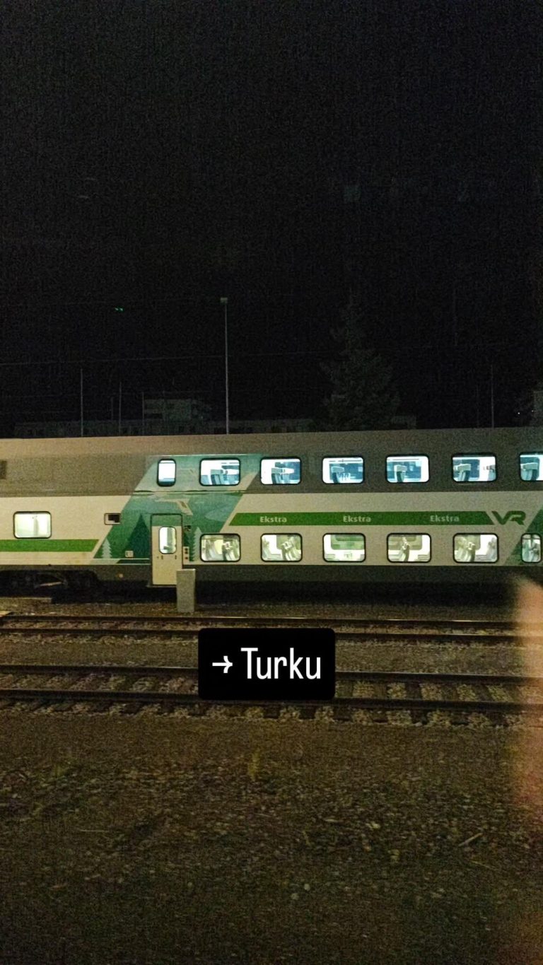 Kuvassa VR:n valkoinen junavaunu, jossa vihreä raita, sekä junaraiteita.