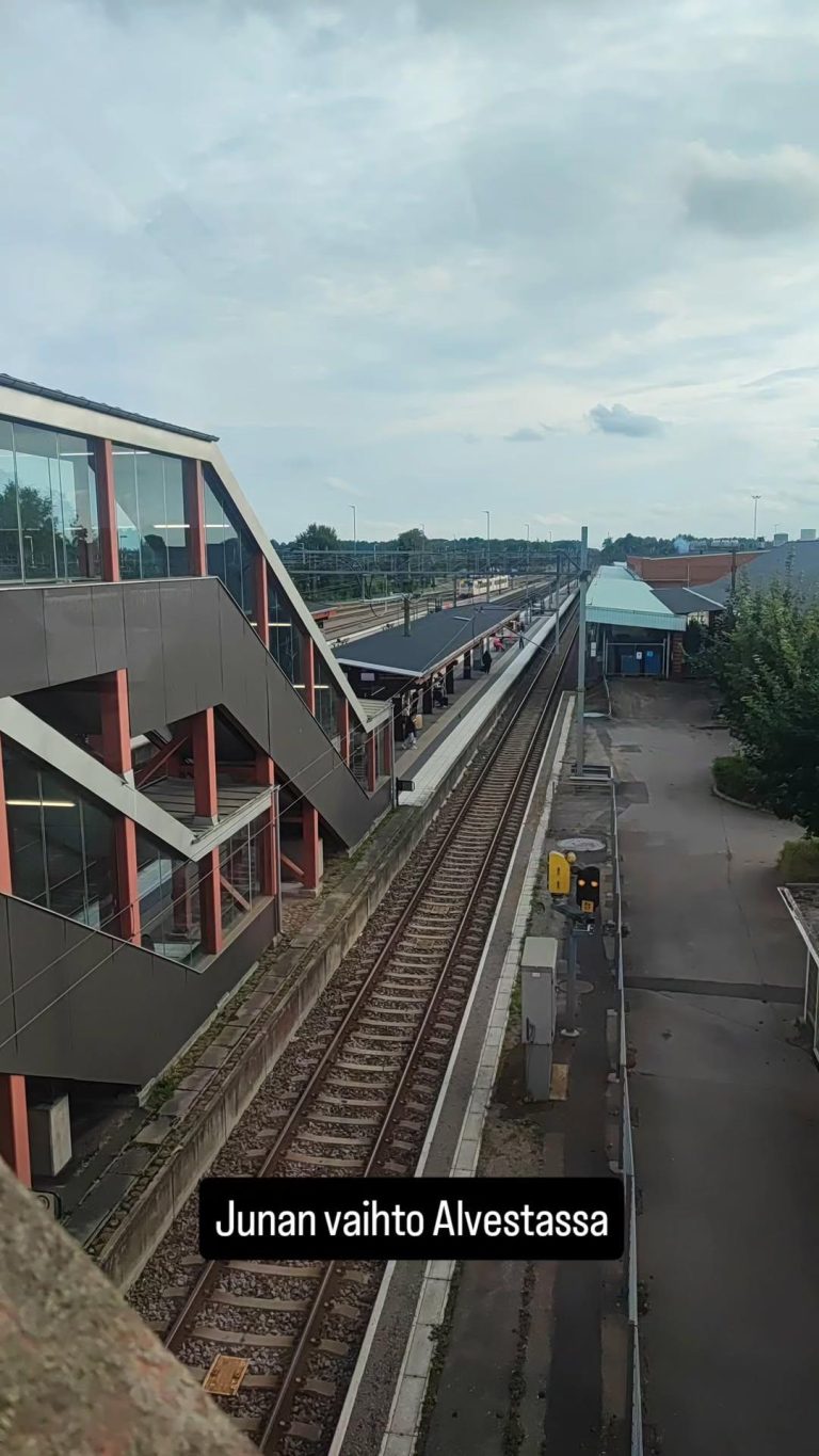 Kuva juna-aseman raiteista ja asemarakennuksen ulkoseinästä. Kuvassa teksti Junan vaihto Alvestassa.