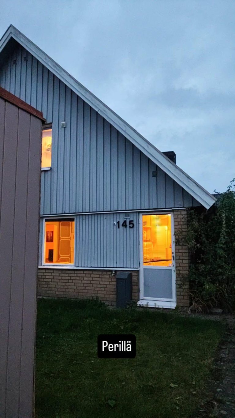 Kuva Växsjössä sijaitsevan talon etuseinästä ja etupihasta. Kuvassa teksti Perillä.