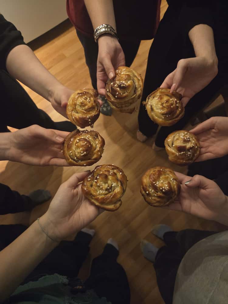 Seitsemän ihmiskättä pitelee seitsemää kanelikierrepullaa ringissä.