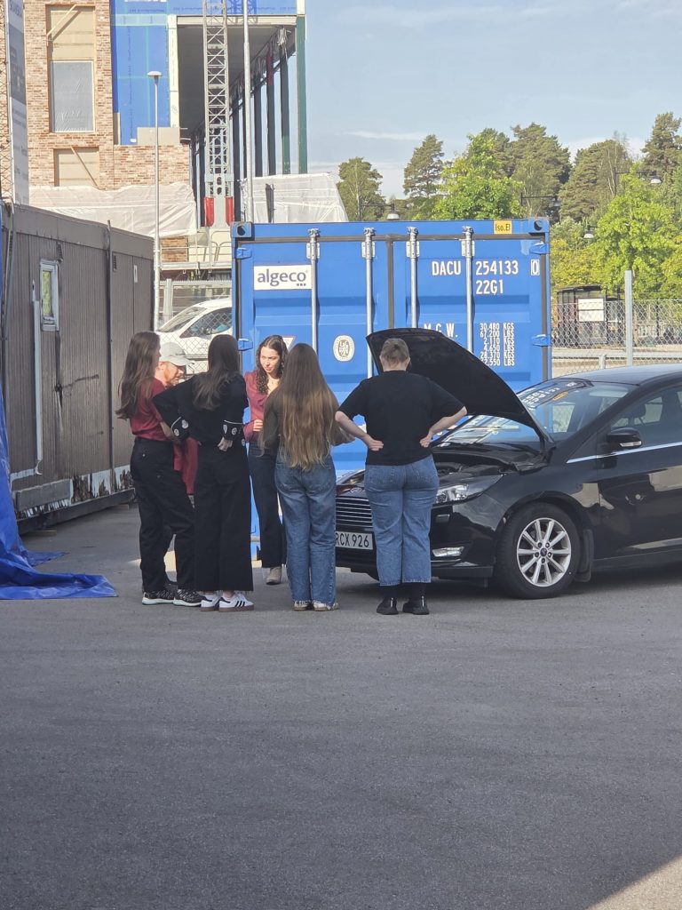 Ryhmä nuoria juttelemassa ja katsomassa autoa, jonka konepelti on auki.