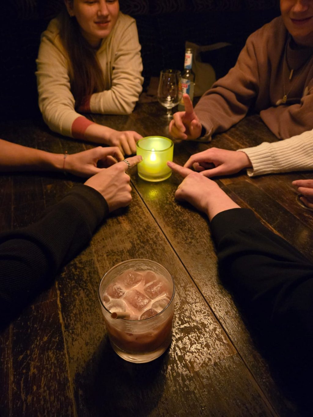 Ihmisiä palavan kynttilän äärellä osoittamassa kynttilätuikkua kohti etusormella.