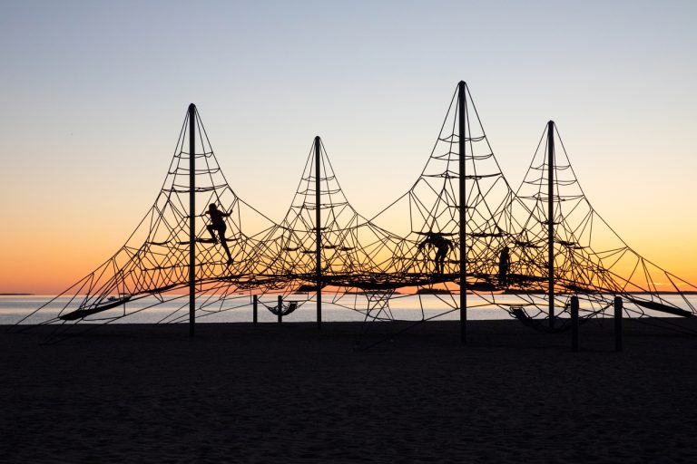 Kuvassa näkyy Nallikarissa sijaitseva suuri kiipeilyteline auringonlaskun aikaan ja kolme mustaa ihmishahmoa vastavalossa.