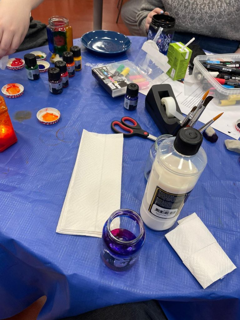 Halloween-teemaisten lasipurkkien maalausta ryhmätoiminnassa.