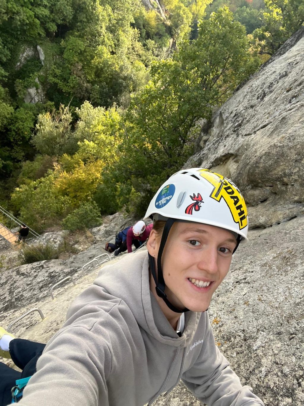 Nuori, kypäräpäinen henkilö kiipeämässä vuoren kallioseinämää.